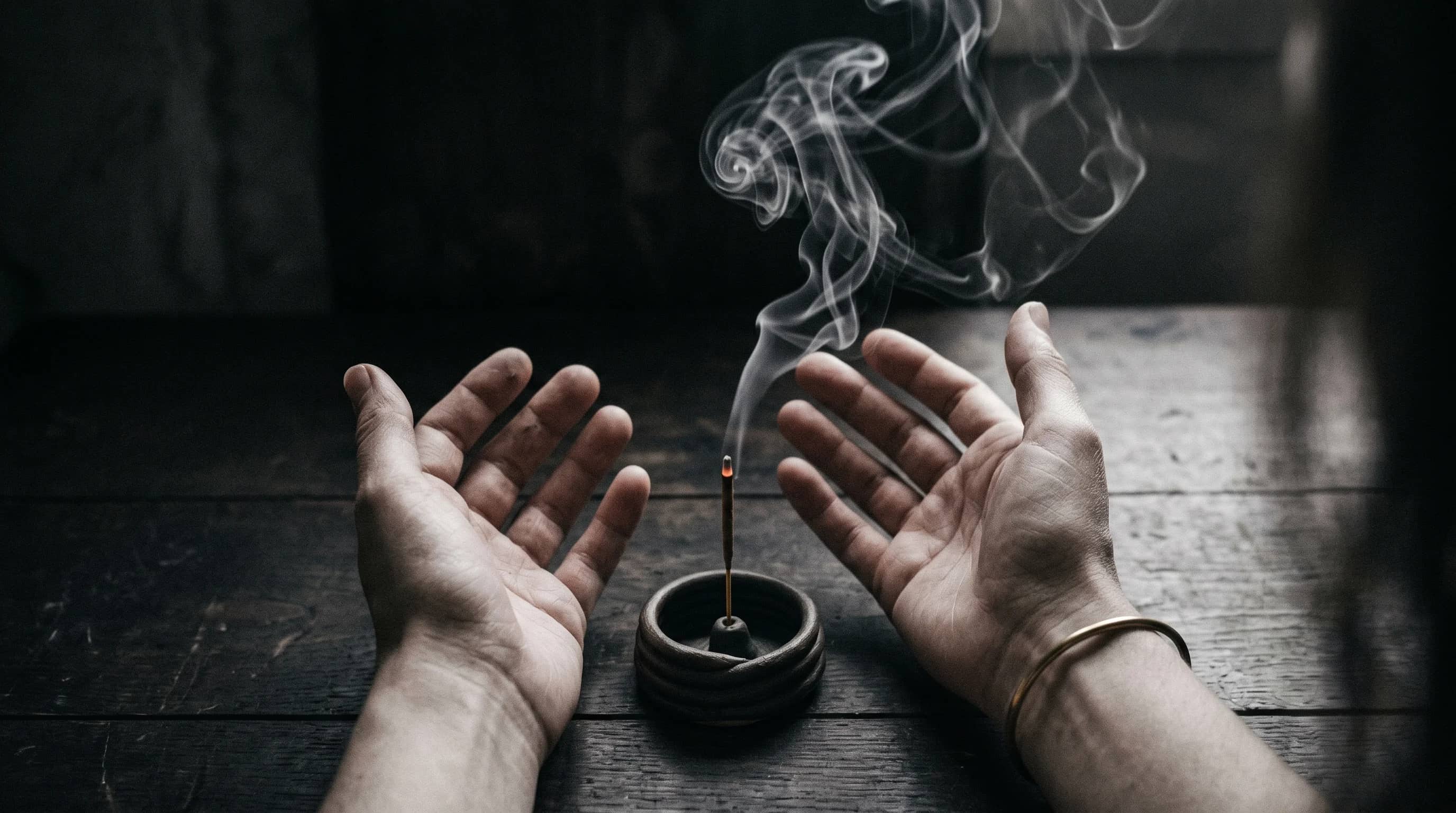 Hands surrounding a fine thread of smoke on a dark table